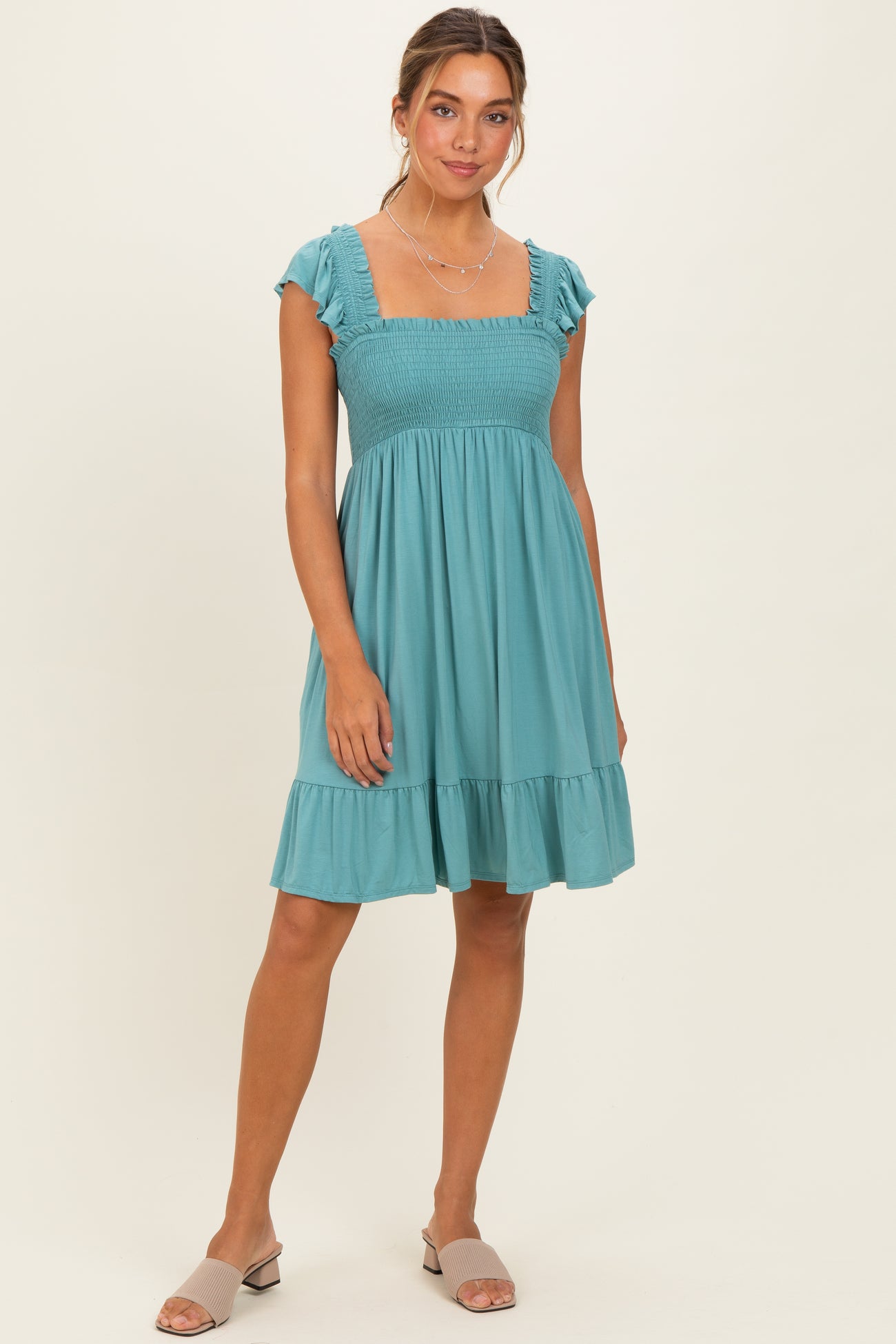 woman wearing a teal off-the-shoulder smocked dress with ruffle sleeves and a tiered hem