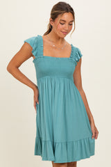 woman wearing a teal smocked dress with ruffled sleeves and a tiered skirt