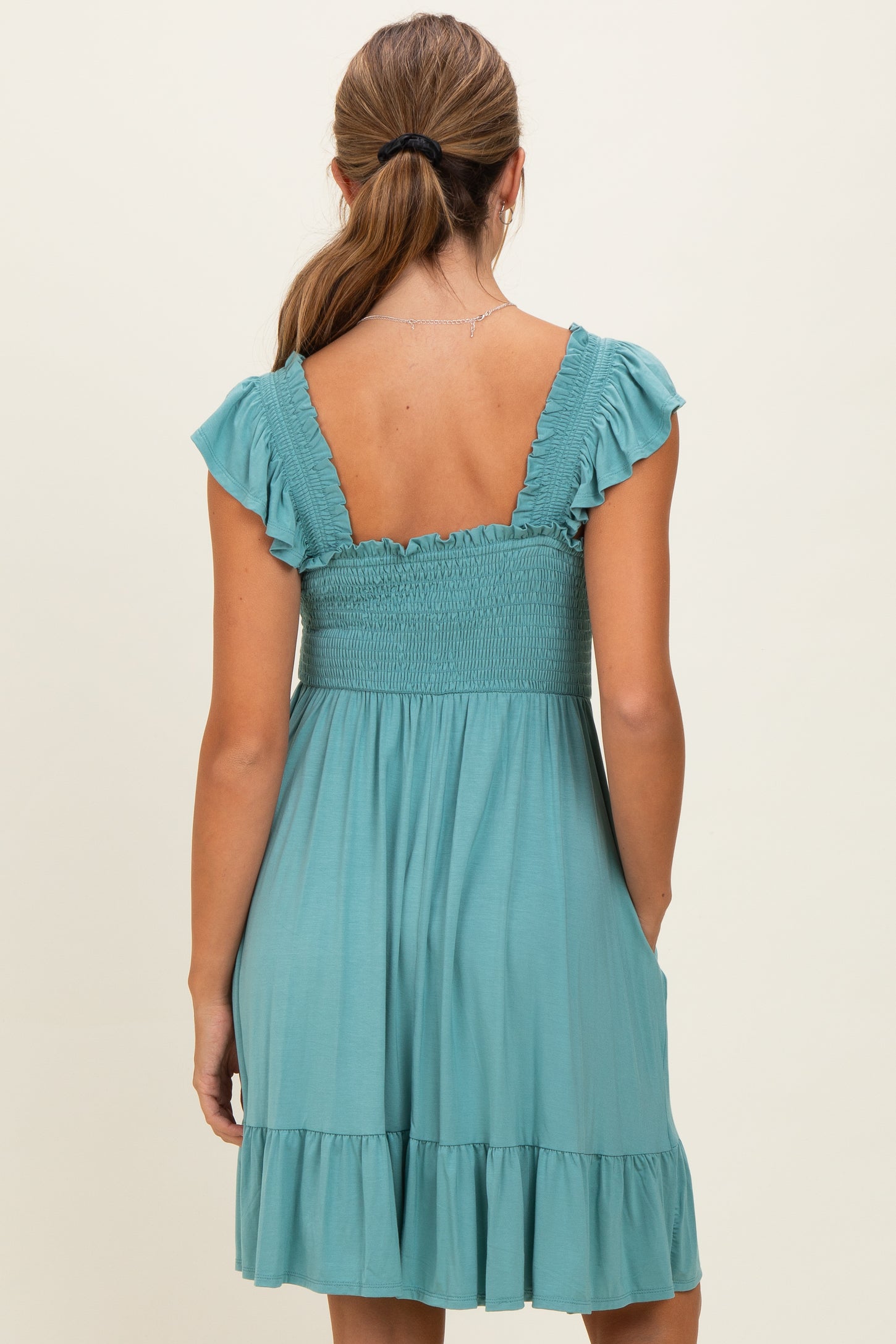 woman wearing a teal smocked back sundress with ruffled sleeves and a flared skirt, showing pockets