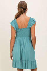 woman wearing a teal smocked back sundress with ruffled sleeves and a flared skirt, showing pockets