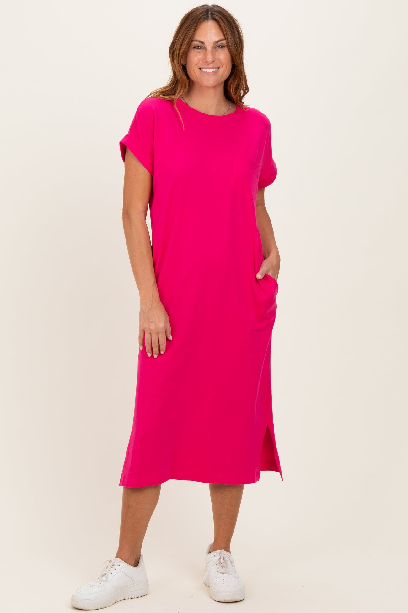 woman wearing a bright pink short sleeve midi dress with pockets and side slits, styled with white sneakers
