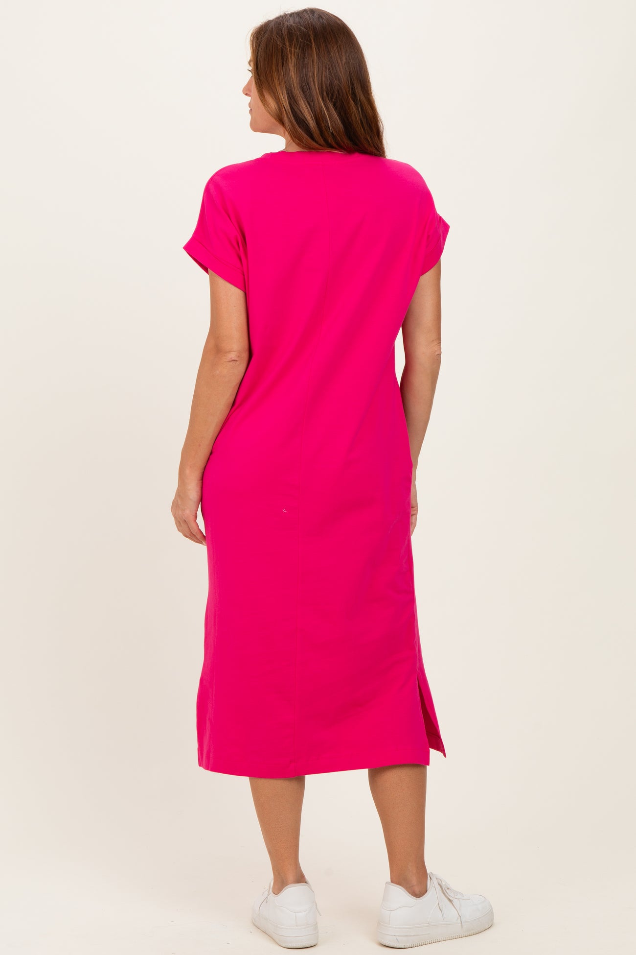 woman wearing a bright pink midi dress with short sleeves and side slits, viewed from the back