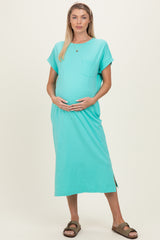 woman wearing a teal maternity dress with short sleeves and a side slit, cradling her baby bump