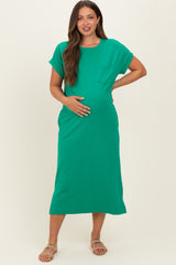 woman wearing a green short sleeve maternity dress with a pocket and holding her baby bump