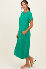 woman wearing a green short sleeve maxi dress with a pocket and side slits, standing with hands in pockets