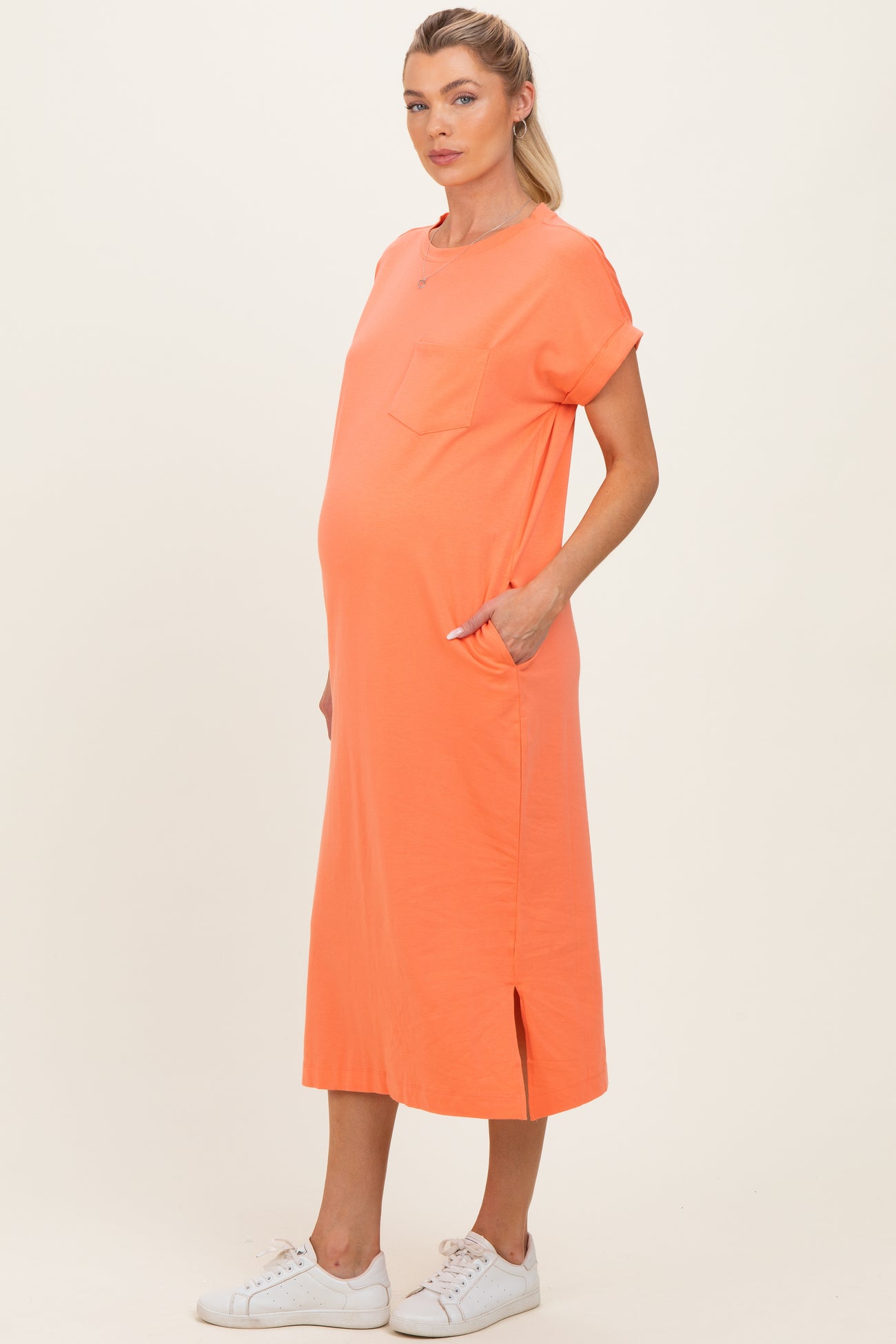 woman wearing an orange maternity dress with short sleeves, pockets, and side slits, showcasing her baby bump