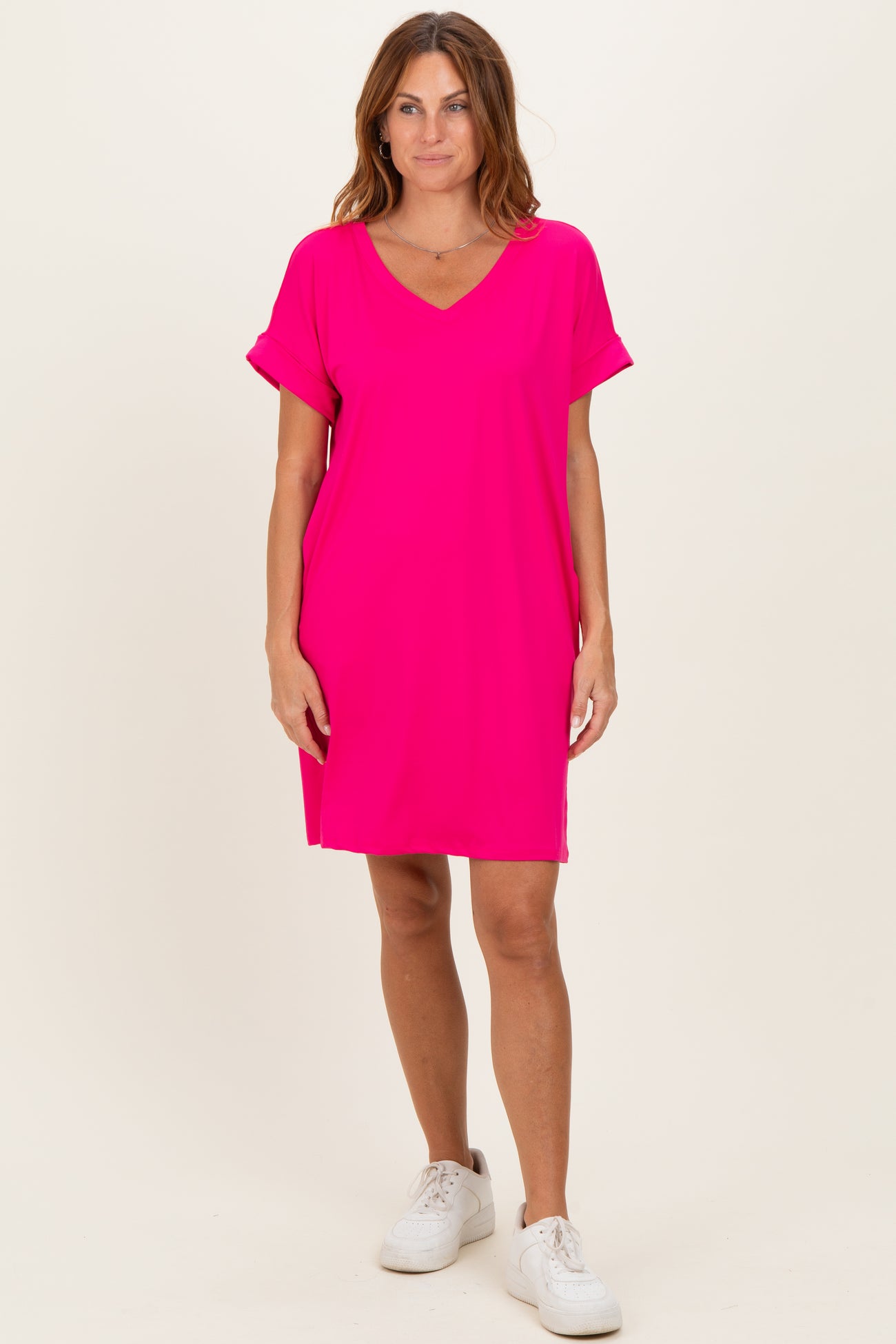 woman wearing a bright pink short sleeve v-neck dress with rolled sleeves and white sneakers