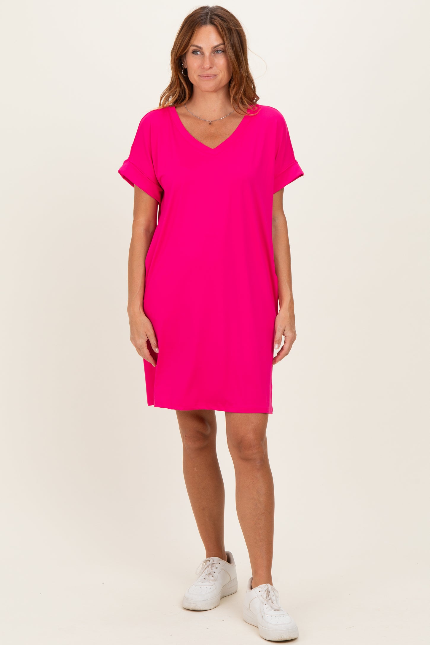 woman wearing a bright pink short sleeve v-neck dress with rolled sleeves and white sneakers