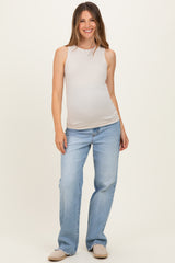 woman wearing a beige maternity tank top and light blue jeans, showing her baby bump