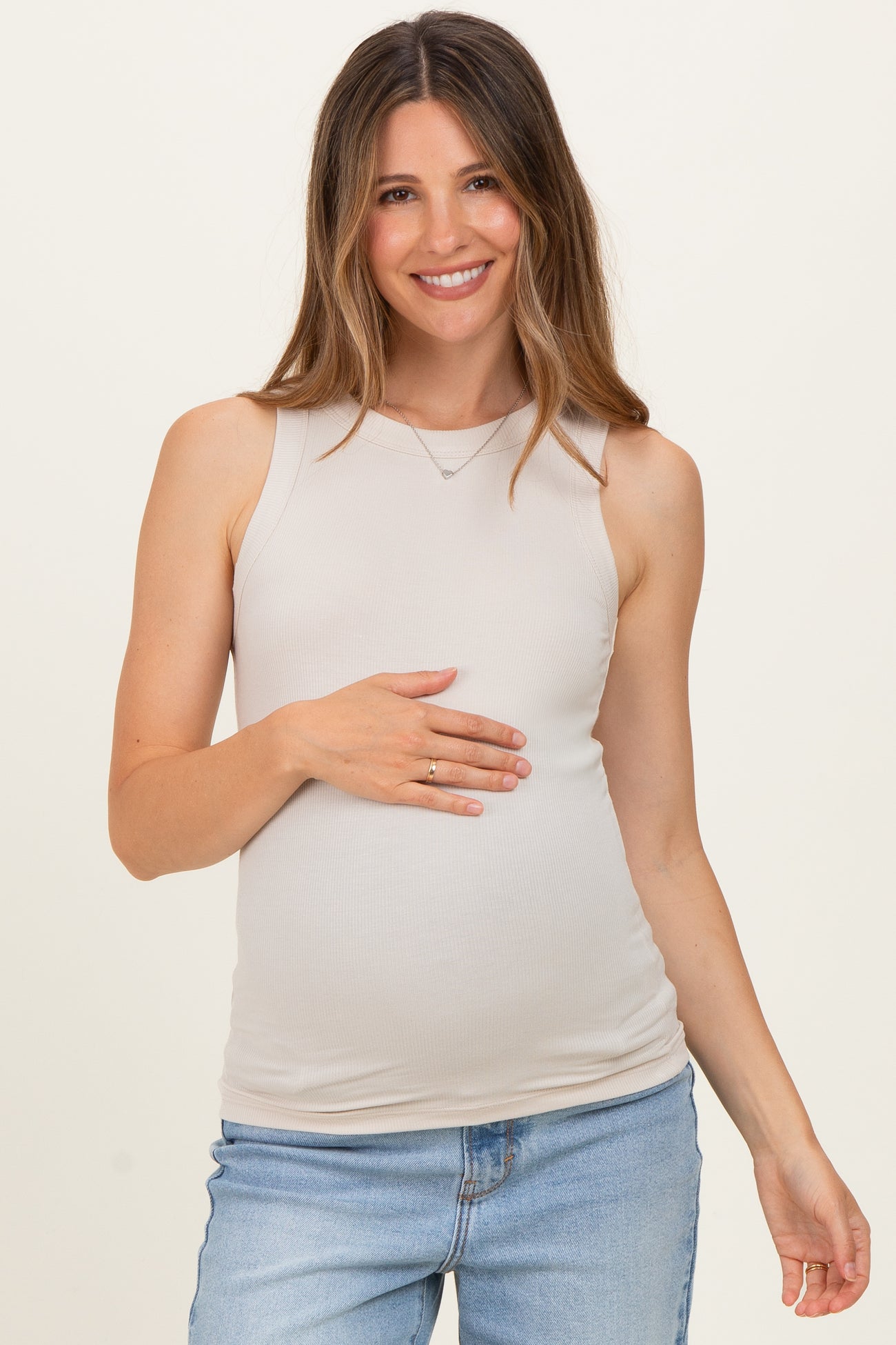 woman wearing a beige maternity tank top and holding her baby bump