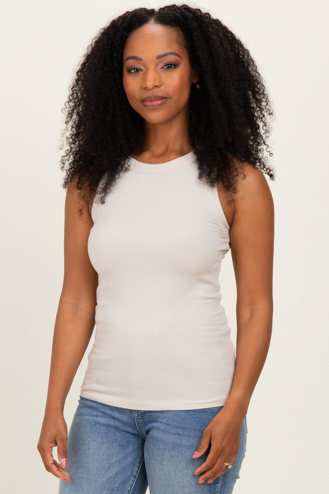 woman wearing a light beige sleeveless ribbed tank top and blue jeans