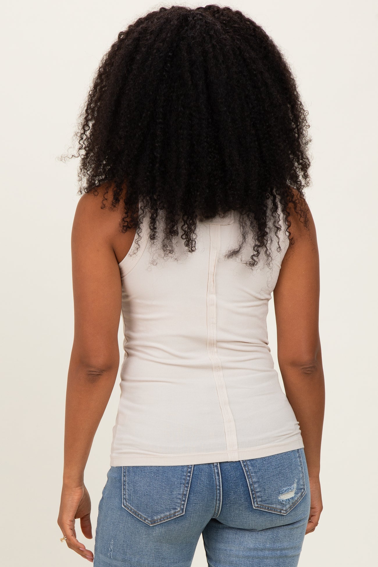 woman wearing a beige fitted tank top with a button detail at the back and blue distressed jeans