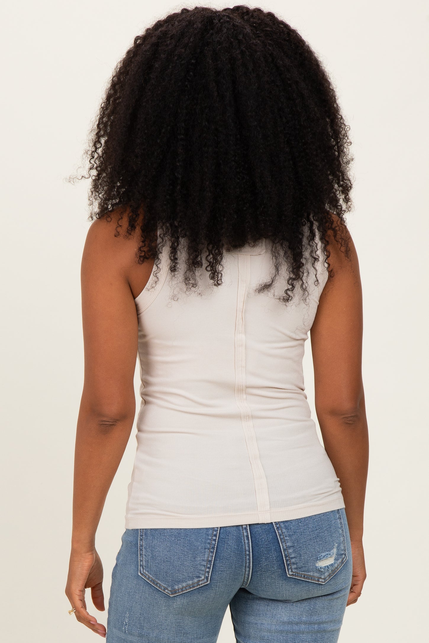 woman wearing a beige fitted tank top with a button detail at the back and blue distressed jeans