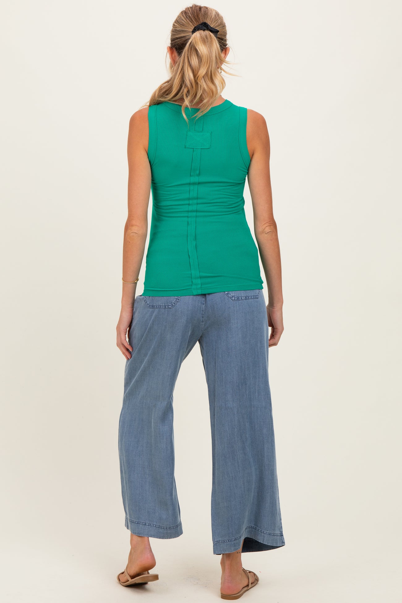 woman wearing a green maternity tank top with gathered detail, paired with light blue wide-leg pants, showing the back view