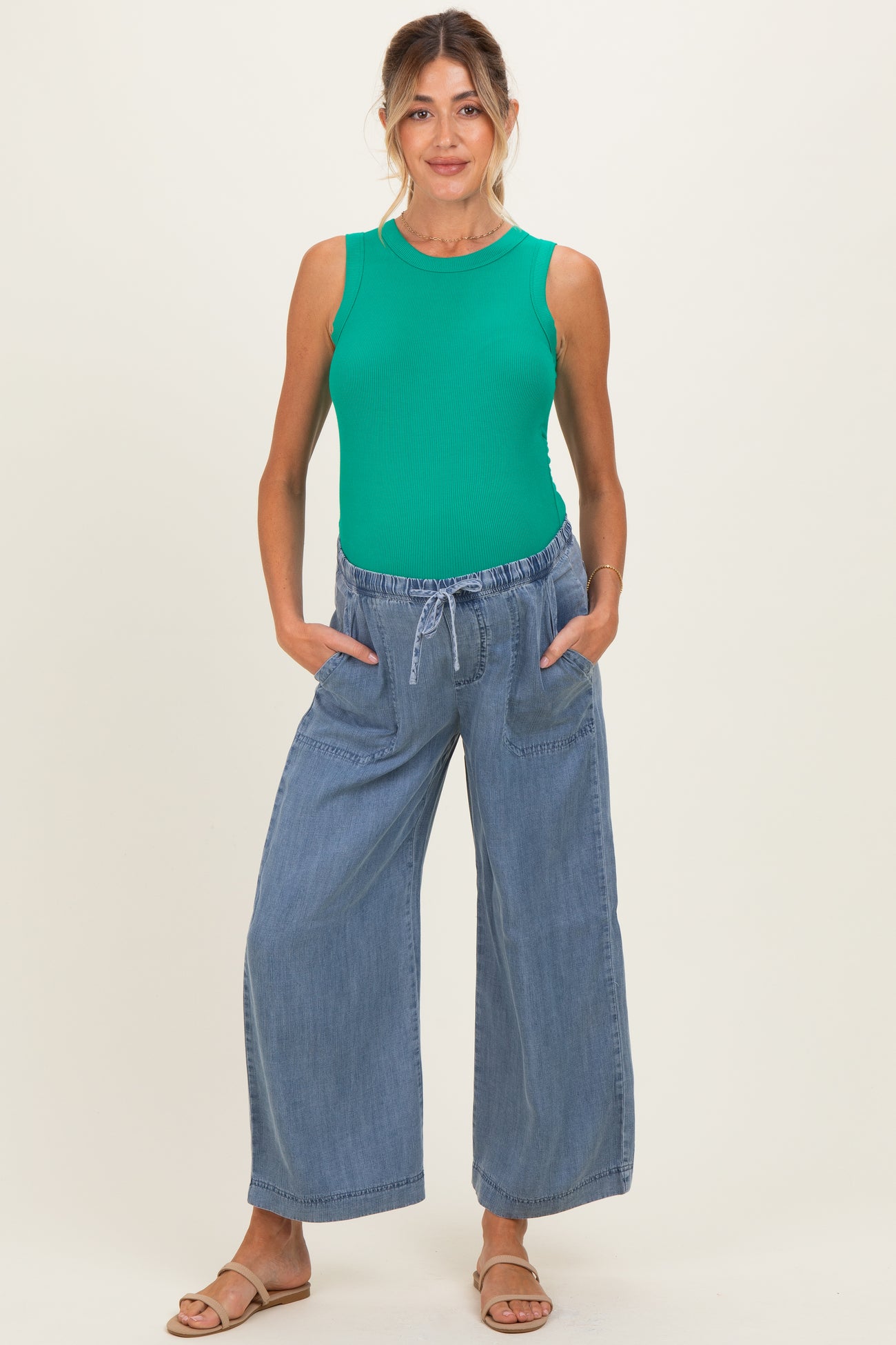 woman wearing a green ribbed maternity tank top and blue wide-leg maternity pants with pockets