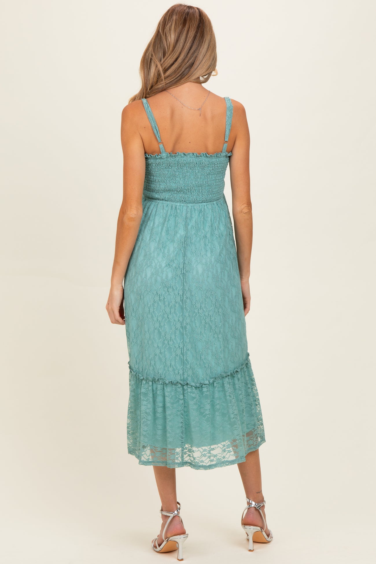 woman wearing a teal lace maternity dress with a smocked bodice and tiered skirt, showing the back view