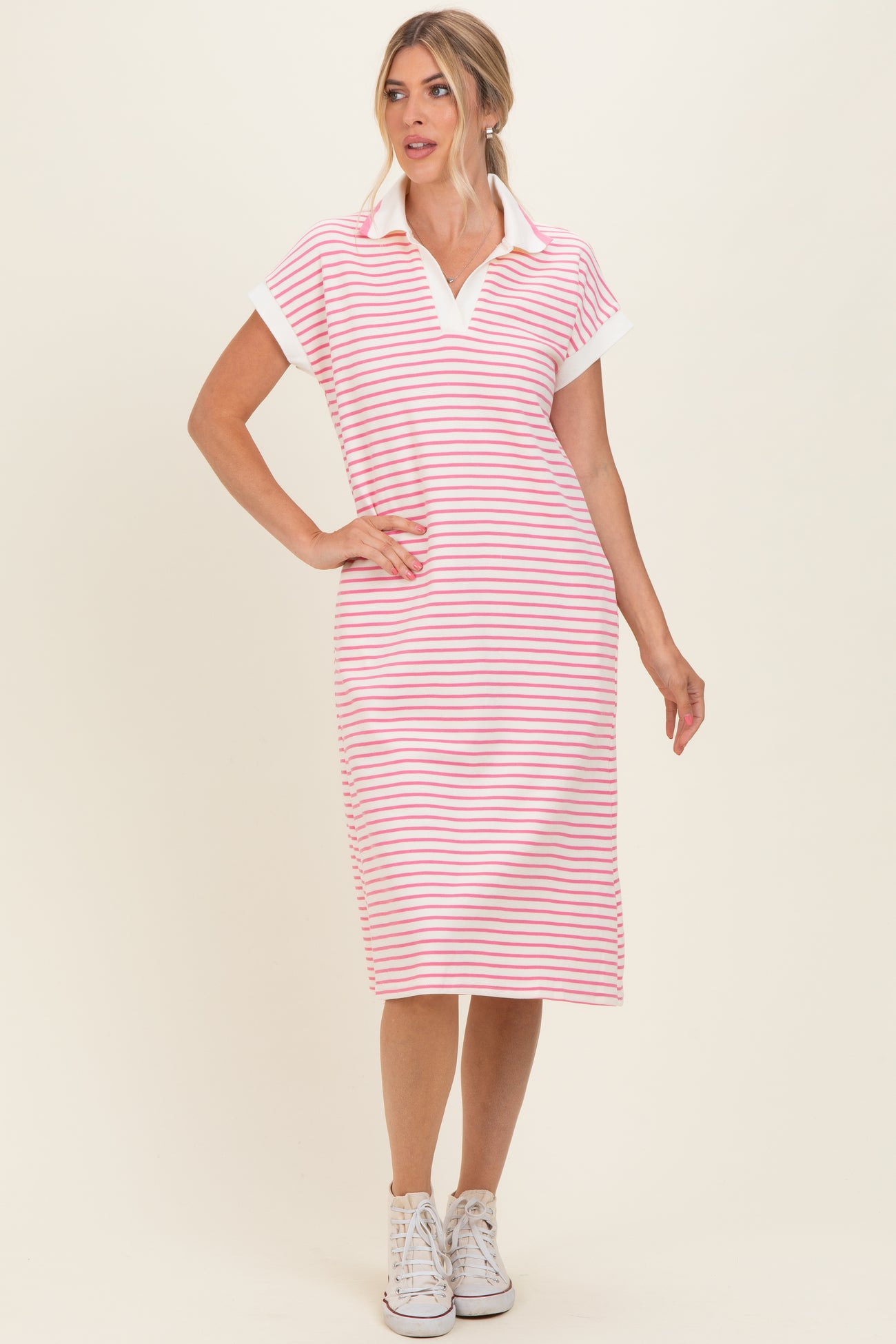 woman wearing a pink and white striped polo midi dress with short sleeves and a collar, styled with white sneakers