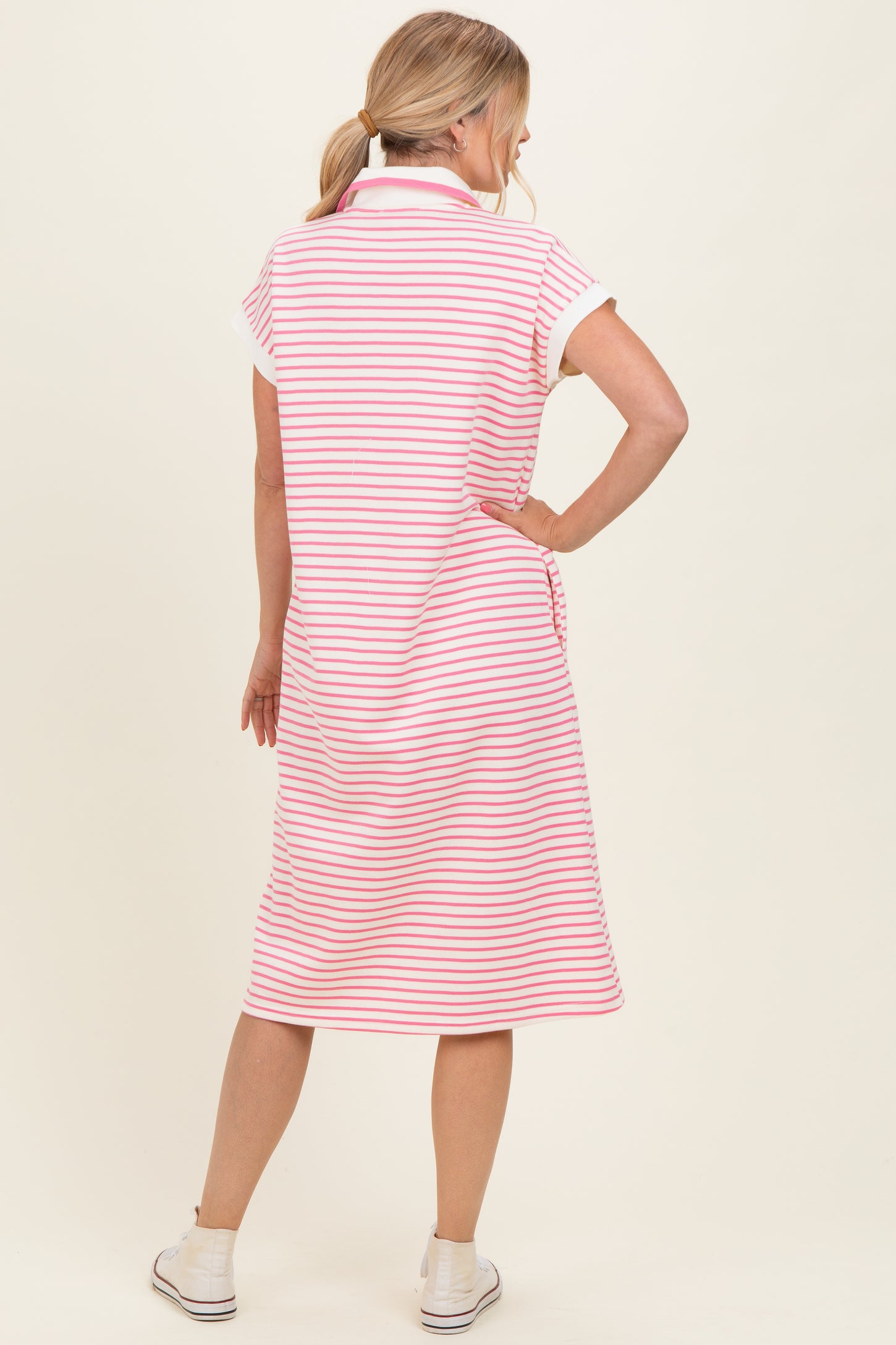 woman wearing a pink and white striped short sleeve polo dress, standing with her back to the camera