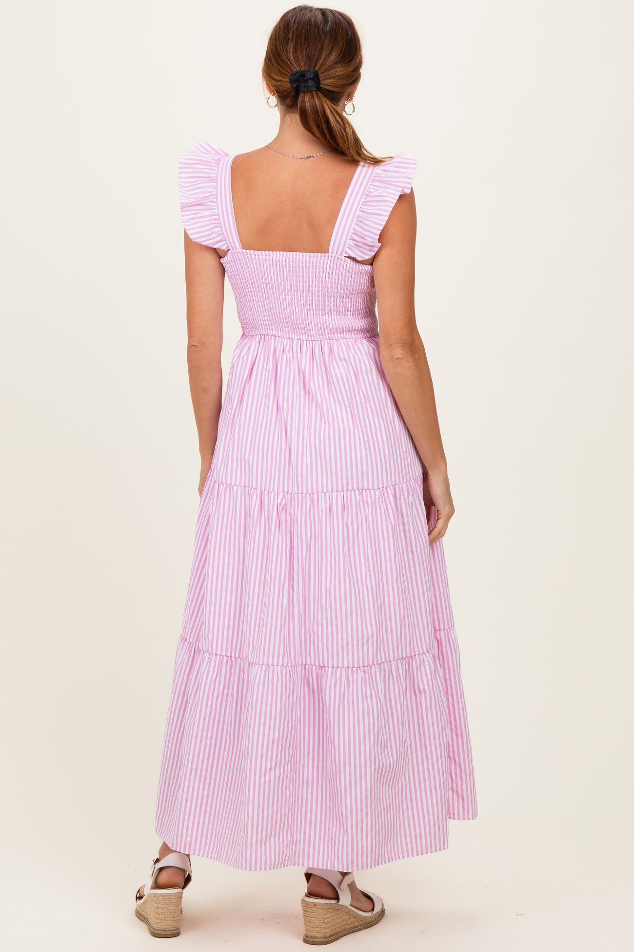 woman wearing a pink and white striped maxi dress with ruffled straps and a smocked bodice, shown from the back