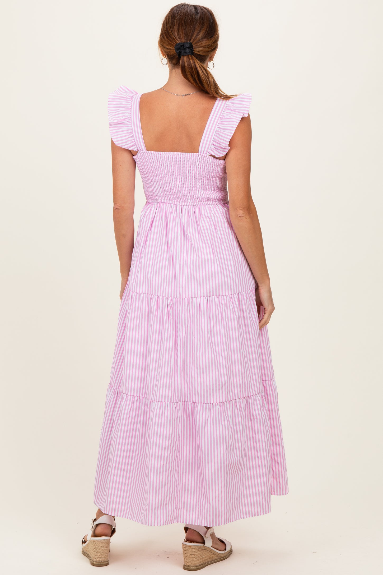 woman wearing a pink and white striped maxi dress with ruffled straps and a smocked bodice, shown from the back