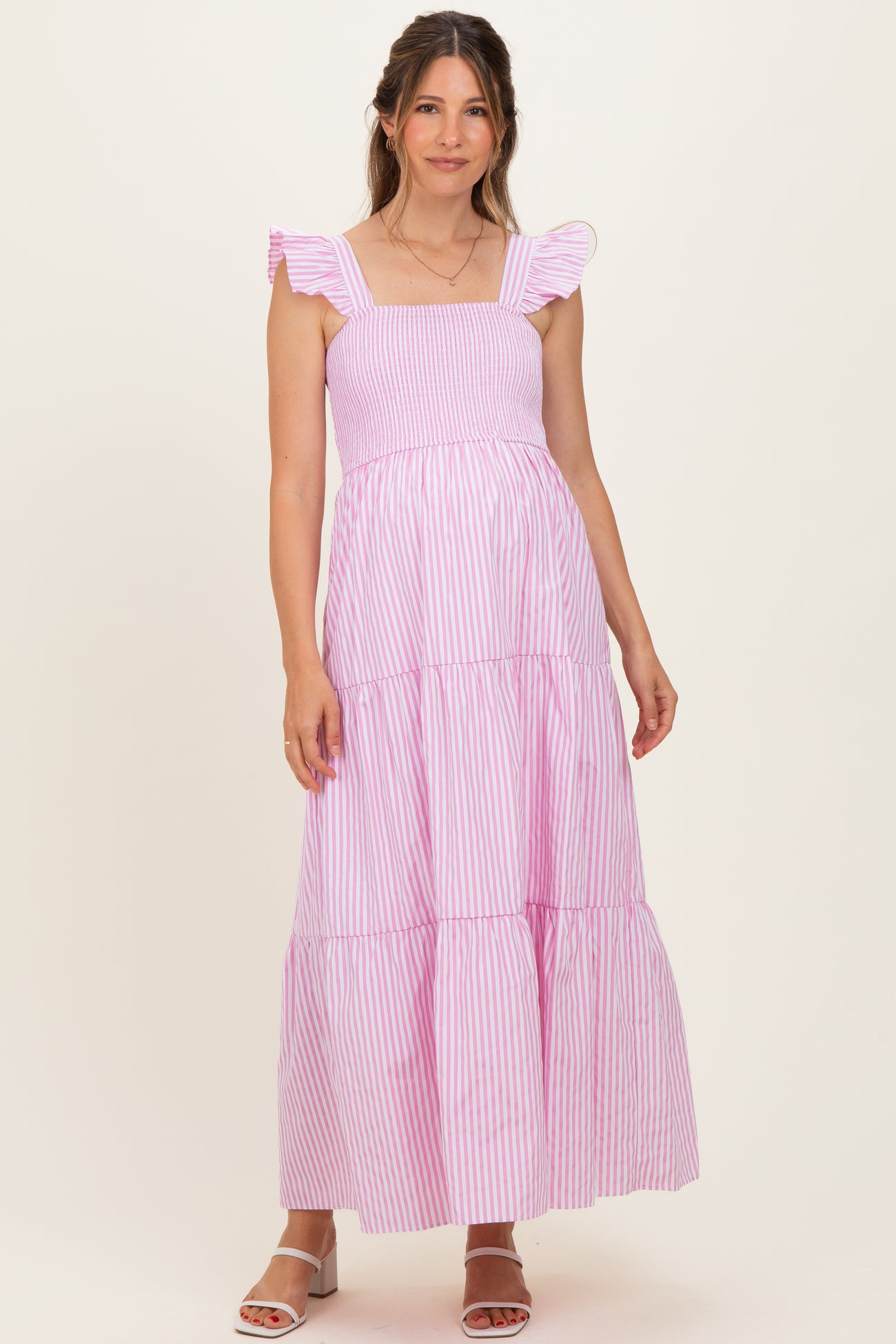 woman wearing a pink and white striped maternity maxi dress with ruffles and a tiered skirt, showing her baby bump