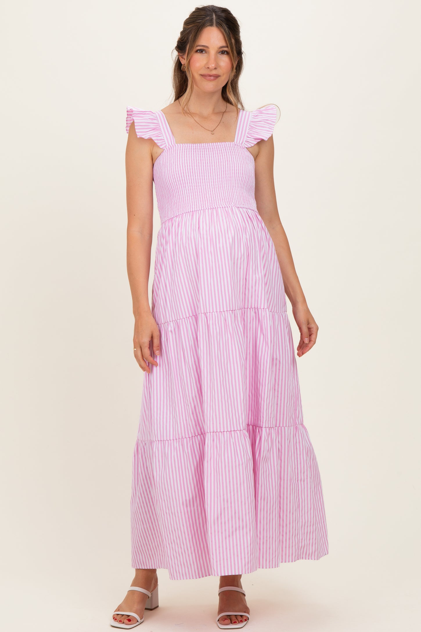 woman wearing a pink and white striped maternity maxi dress with ruffles and a tiered skirt, showing her baby bump