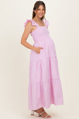 woman wearing a pink and white striped maternity maxi dress with ruffle straps and pockets, showcasing her baby bump