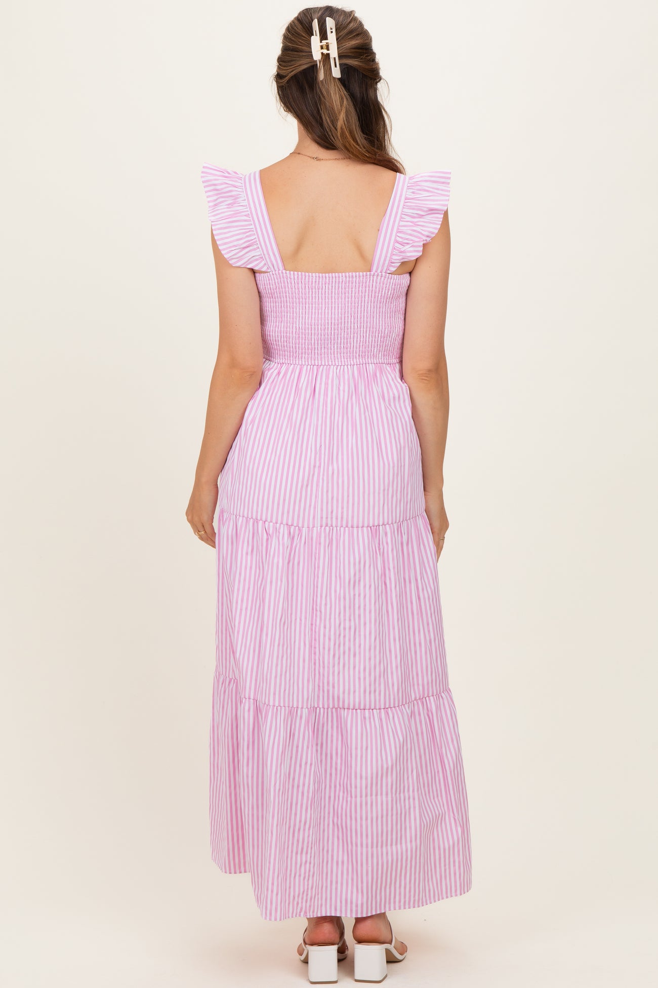 woman wearing a pink and white striped maternity dress with ruffle sleeves and a tiered skirt from the back