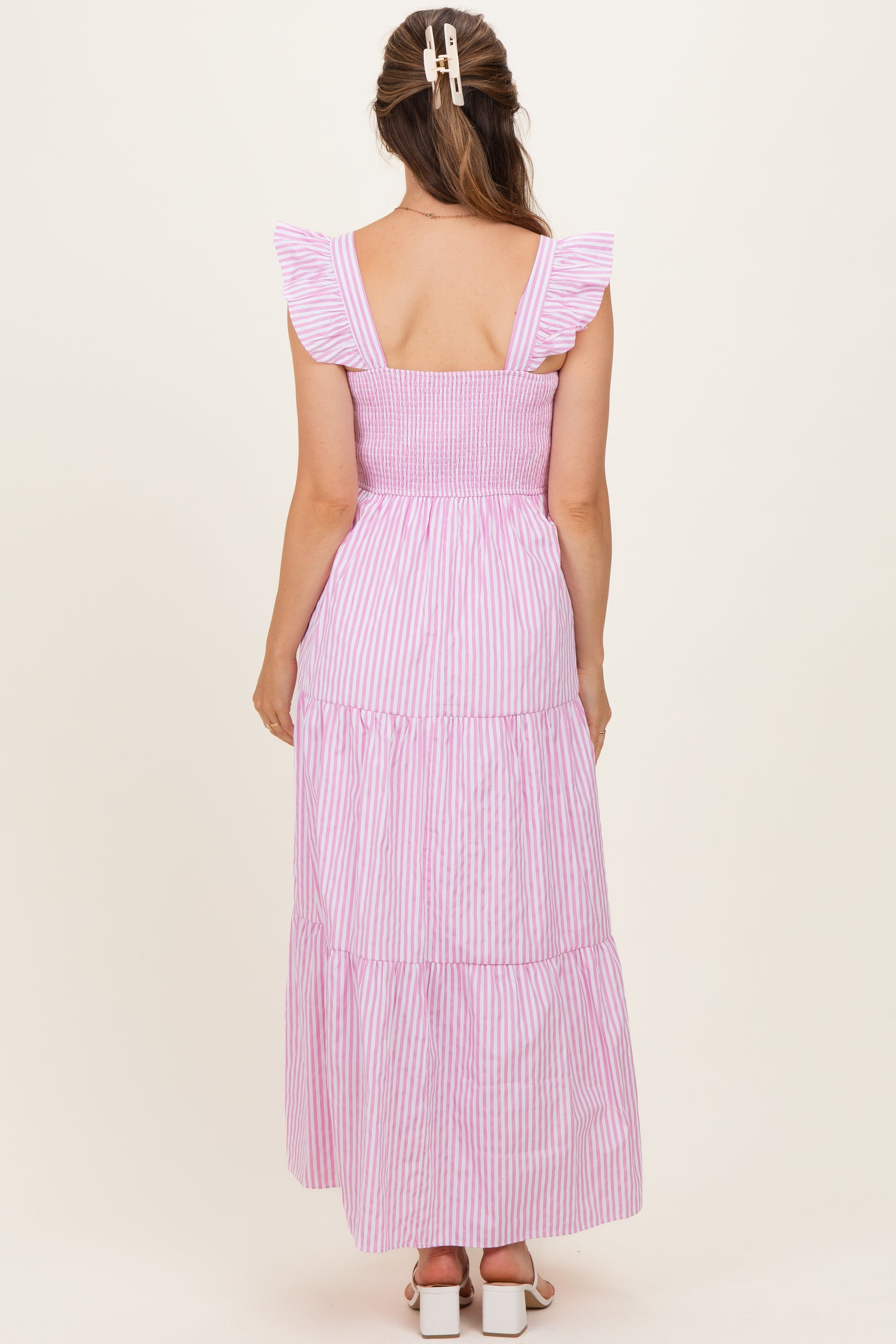 woman wearing a pink and white striped maternity dress with ruffle sleeves and a tiered skirt from the back