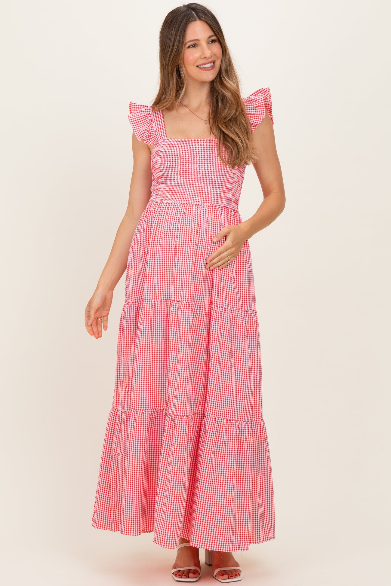 woman wearing a red and white gingham maternity maxi dress with ruffled straps and tiered detailing, holding her baby bump