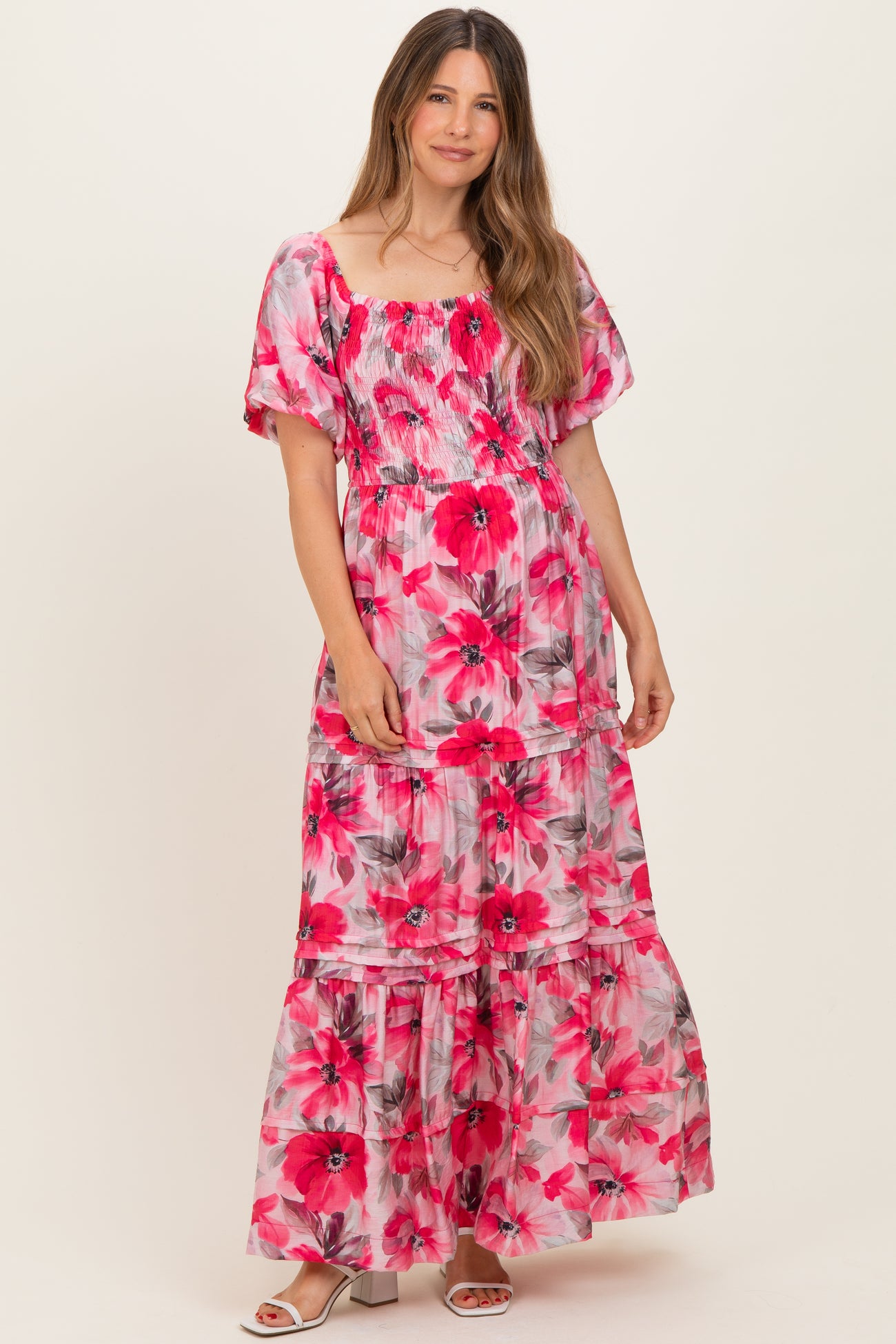 woman wearing a pink floral maternity maxi dress with puff sleeves and a tiered skirt, showcasing her baby bump