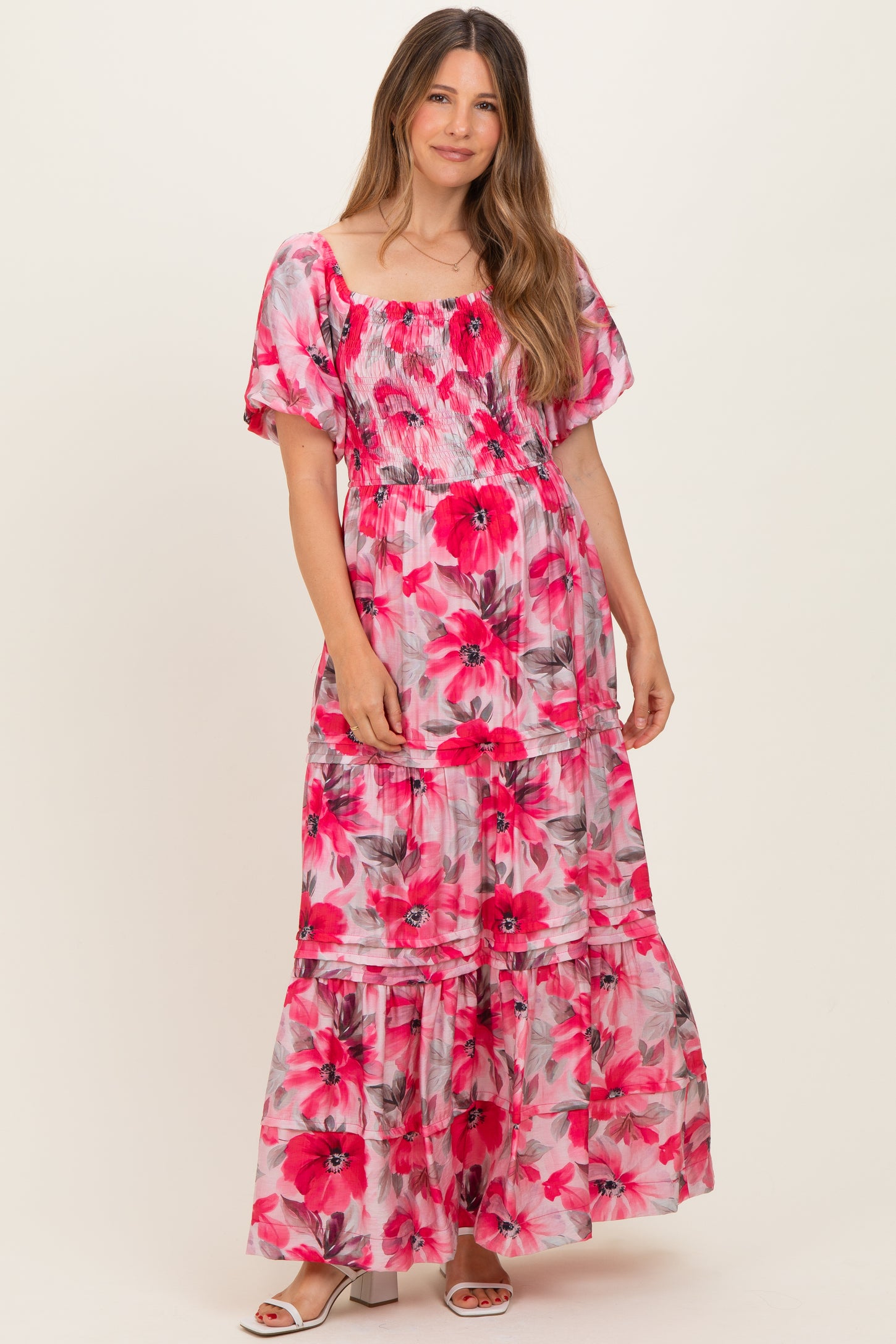 woman wearing a pink floral maternity maxi dress with puff sleeves and a tiered skirt, showcasing her baby bump