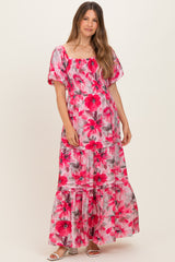 woman wearing a pink floral maternity maxi dress with puff sleeves and a tiered skirt, showcasing her baby bump