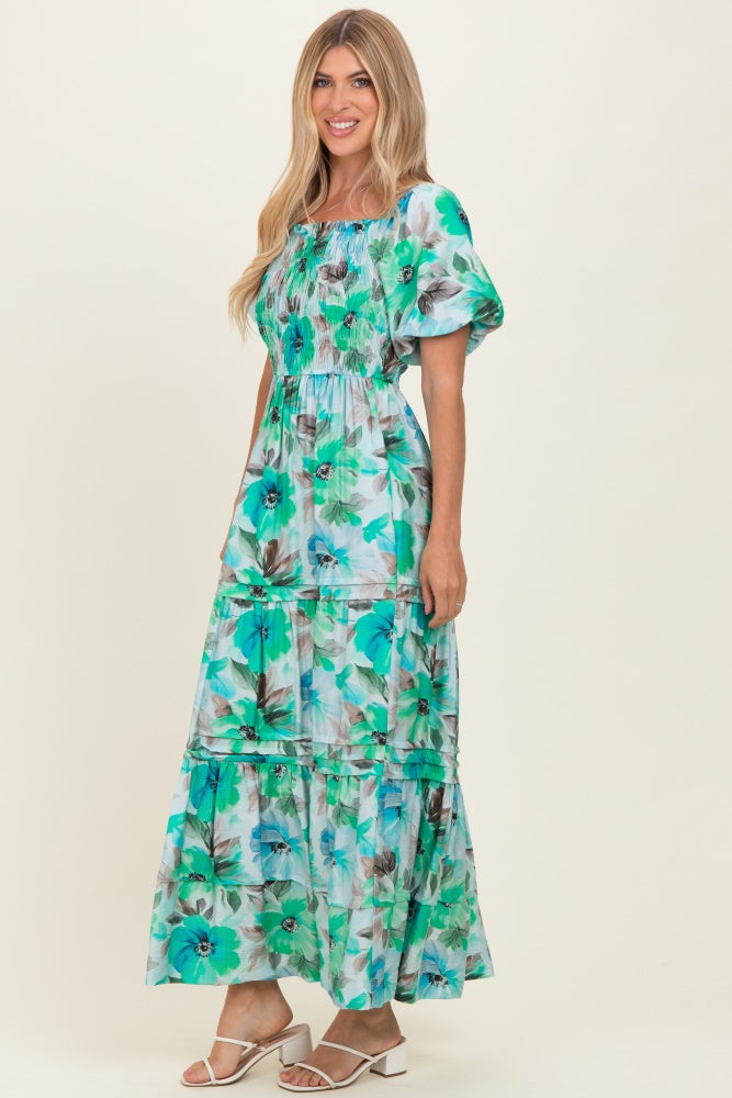 woman wearing a floral print maxi dress in teal and green with puff sleeves and a tiered skirt