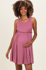 woman wearing a mauve ribbed maternity dress with a ruffled waist, gently holding her baby bump