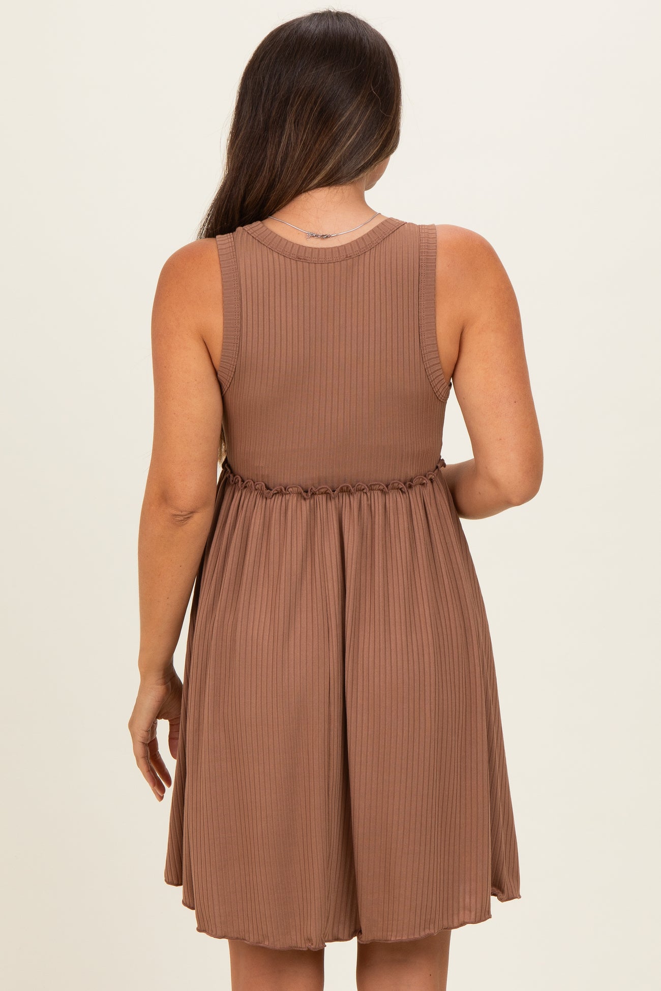 woman wearing a brown sleeveless maternity dress with a pleated design and an elastic waistband