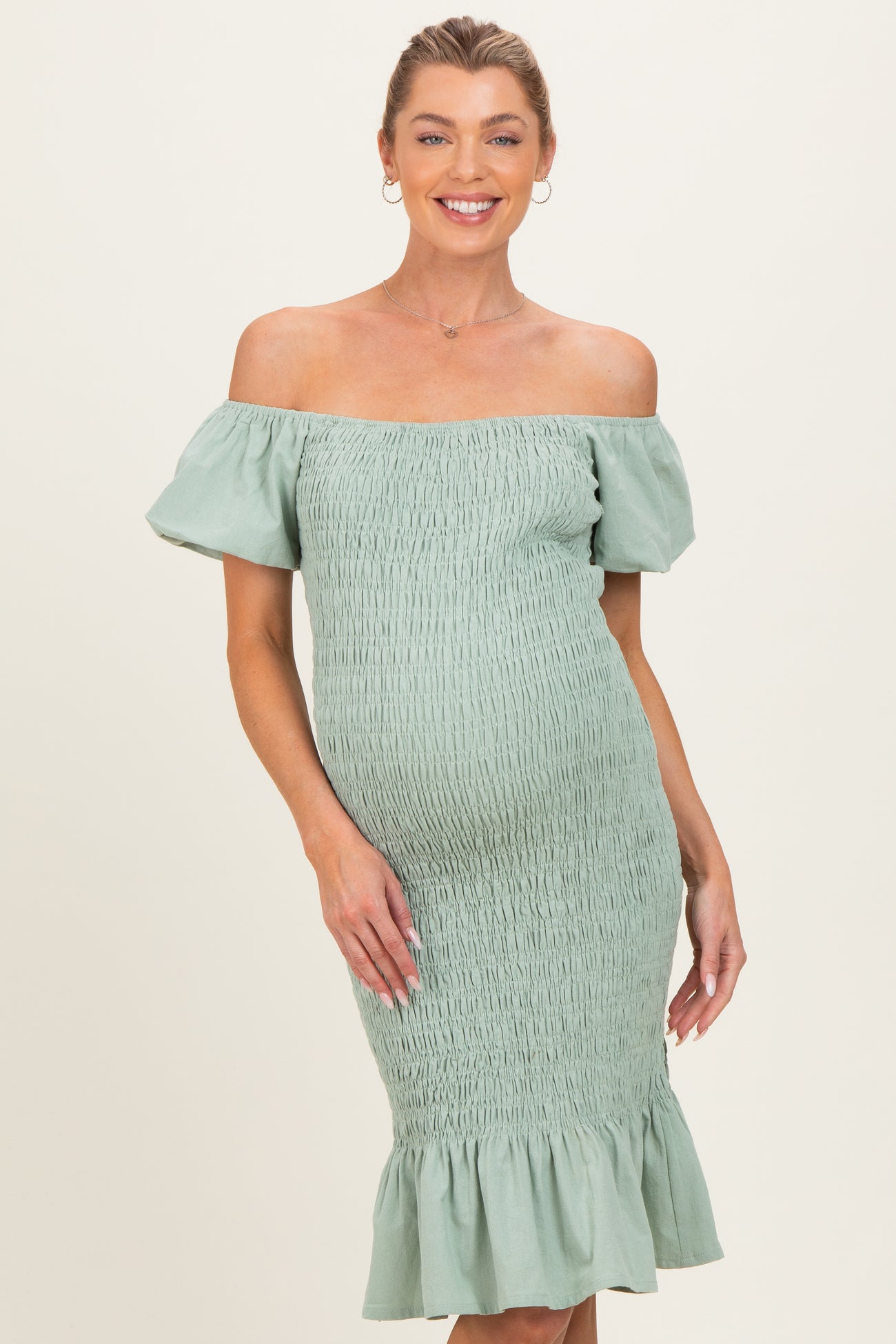 woman wearing a light green off-the-shoulder maternity dress with smocking and ruffled hem, showcasing her baby bump