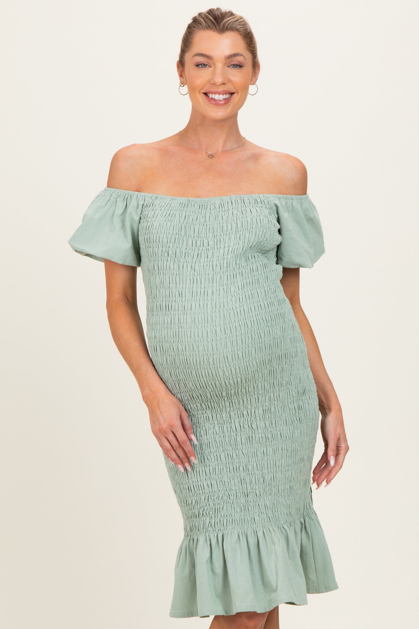 woman wearing a light green off-the-shoulder maternity dress with smocking and ruffled hem, showcasing her baby bump