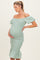 woman wearing a light green off-the-shoulder maternity dress with a fitted silhouette and ruffled hem, cradling her baby bump
