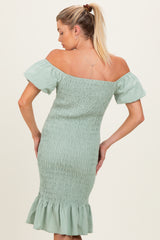 woman wearing a light green off-the-shoulder maternity dress with ruffled hem and smocked detailing, showing her back