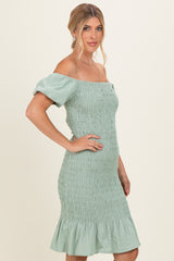 woman wearing a mint green smocked off-the-shoulder dress with short puff sleeves and a flared hem