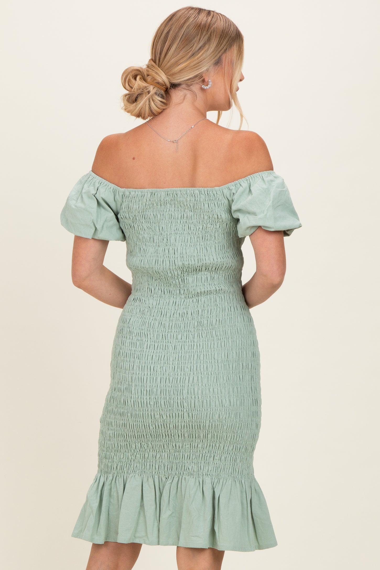 woman wearing a sage green off-the-shoulder fitted dress with smocked bodice and ruffled hem