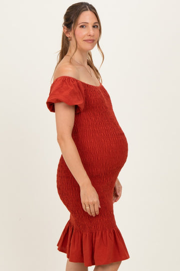 woman wearing a rust off-the-shoulder maternity dress with a ruffled hem and visible baby bump