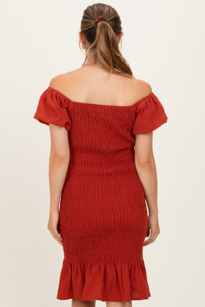 woman wearing a rust off-the-shoulder maternity dress with smocked detailing and a ruffled hem, showing her back
