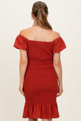 woman wearing a rust off-the-shoulder maternity dress with smocked detailing and a ruffled hem, showing her back