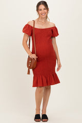 woman wearing a rust off-the-shoulder maternity dress with puff sleeves and a ruffled hem, carrying a brown crossbody bag