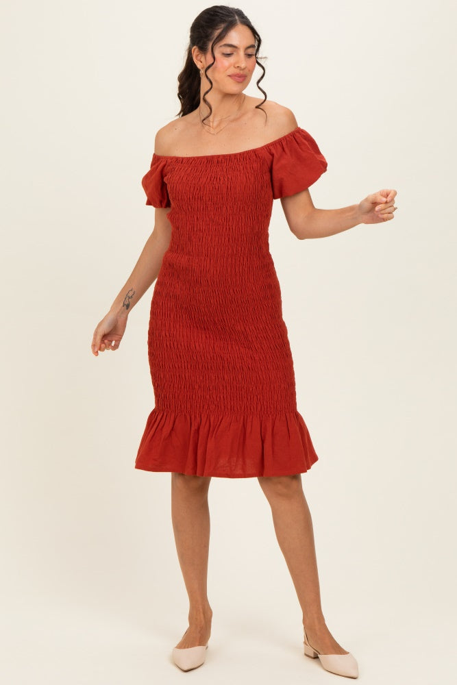 woman wearing a rust red off-the-shoulder knee-length dress with smocked bodice and ruffled hem