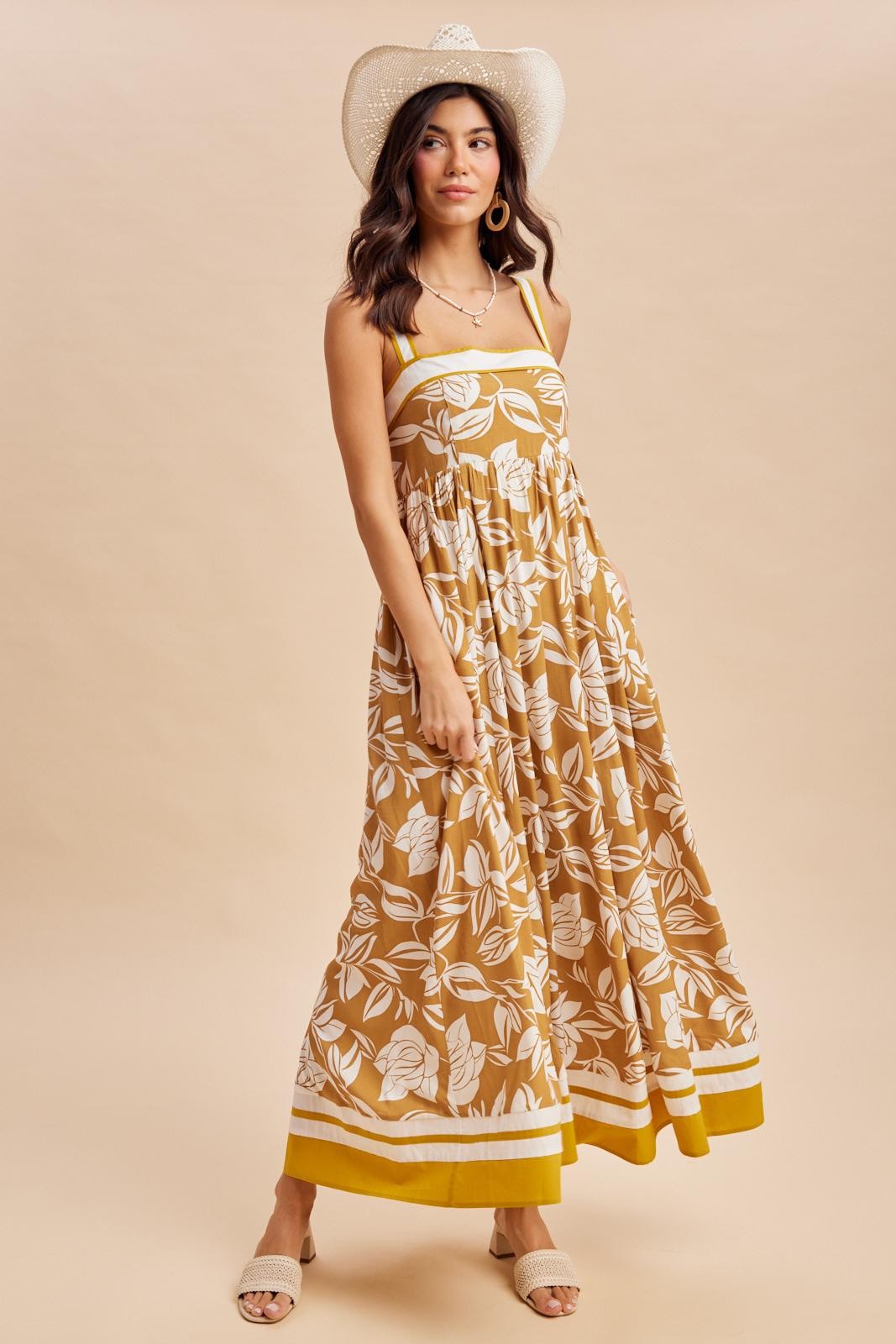 woman wearing a mustard yellow floral maxi dress with a fitted bodice and flowing skirt, accessorized with a straw hat