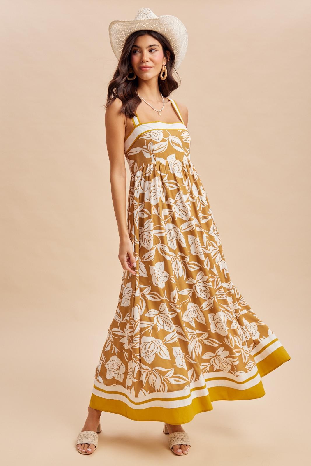woman wearing a mustard yellow floral maxi dress with a fitted bodice and flowy skirt, styled with a white cowboy hat