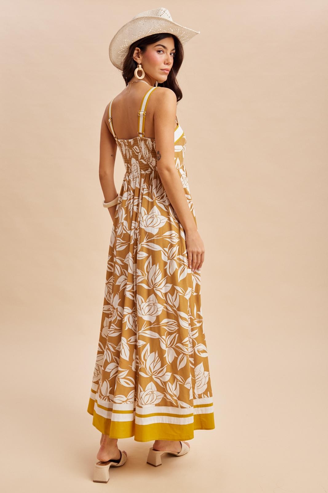 woman wearing a brown floral maxi dress with spaghetti straps and a gathered back, accessorized with a wide-brimmed hat